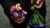 Un devoto sostiene una vela encendida en su mano y un ramo de flores moradas, en tributo a San Lázaro. 